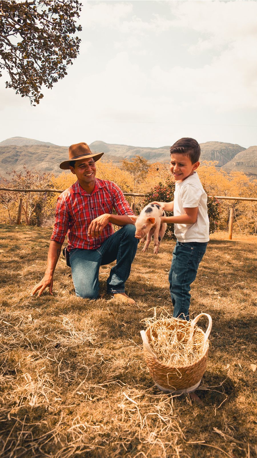 Peão e criança com um leitãozinho nas mãos, no pasto da mini fazenda