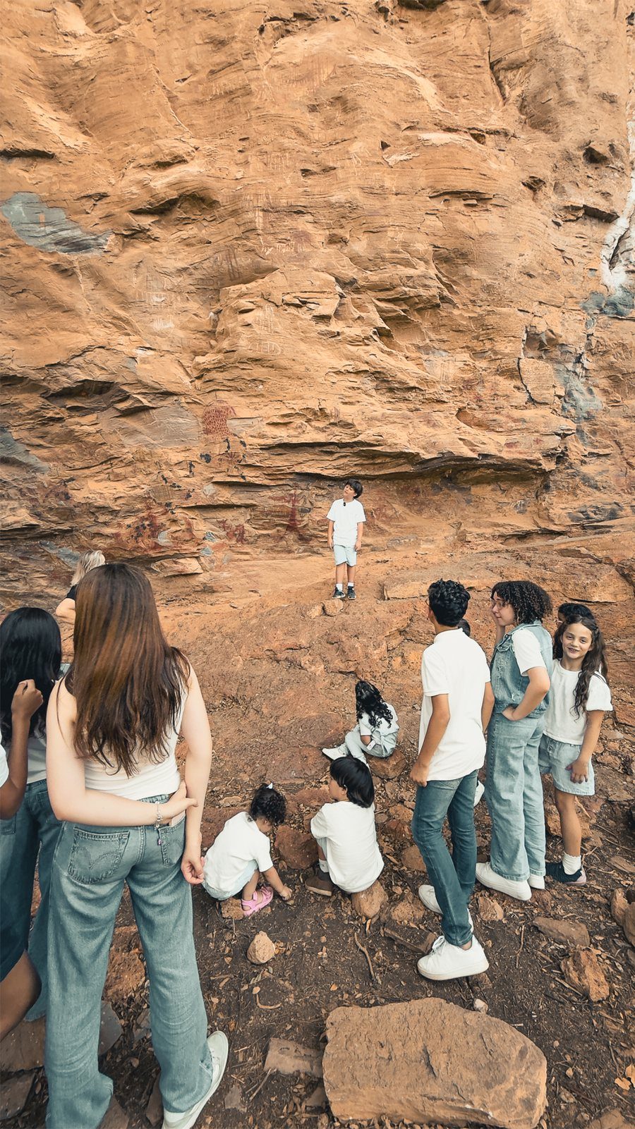 Visitantes sentados diante do abrigo de pedra do sítio arqueológico